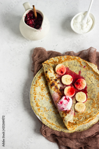 Vanilla poppy seed pancakes or crepes with natural yogurt, banana and cherry sauce with spices (cinnamon and anise). Light concrete background. Copy space.