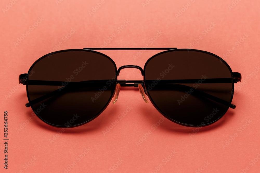 Close-up sunglasses on coral background. Top view. Flat lay. Copy space. New minimal creative concept. Summer is coming concept. Living Coral color of the Year 2019 Close-up sunglasses on coral background. Top view. Flat lay. Copy space. New minimal creative concept. Summer is coming concept. Living Coral color of the Year 2019
