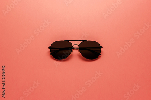 Black sunglasses on coral background. Top view. Flat lay. Copy space. Minimal style with colorful paper backdrop. Summer is coming concept. Living Coral color of the Year 2019