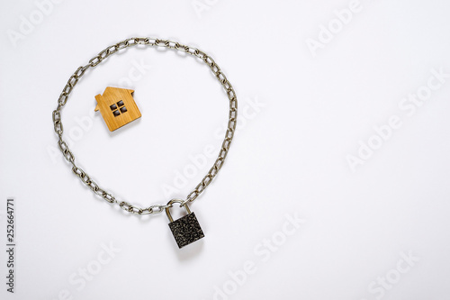 Imitation of a house made of wood fenced with a metal chain with a lock on a white background.