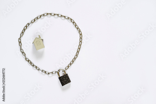 Imitation of a house made of metal fenced with a metal chain with a lock on a white background.