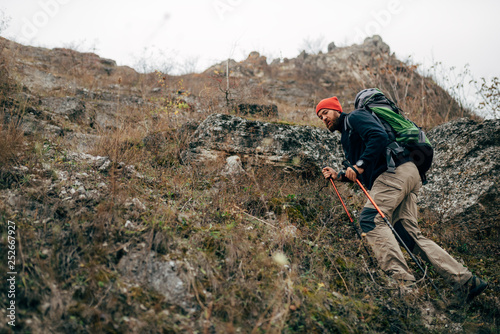 Young active male hiking in mountains with travel backpack. Traveler bearded man trekking and mountaineering during his journey. Travel, people, sport and healthy lifestyle concept