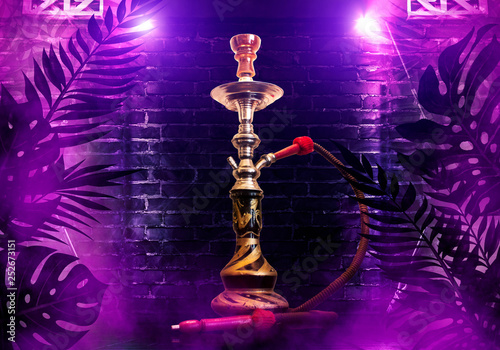 Hookah on the background of tropical leaves and a brick wall. Neon light, laser figures in smoke