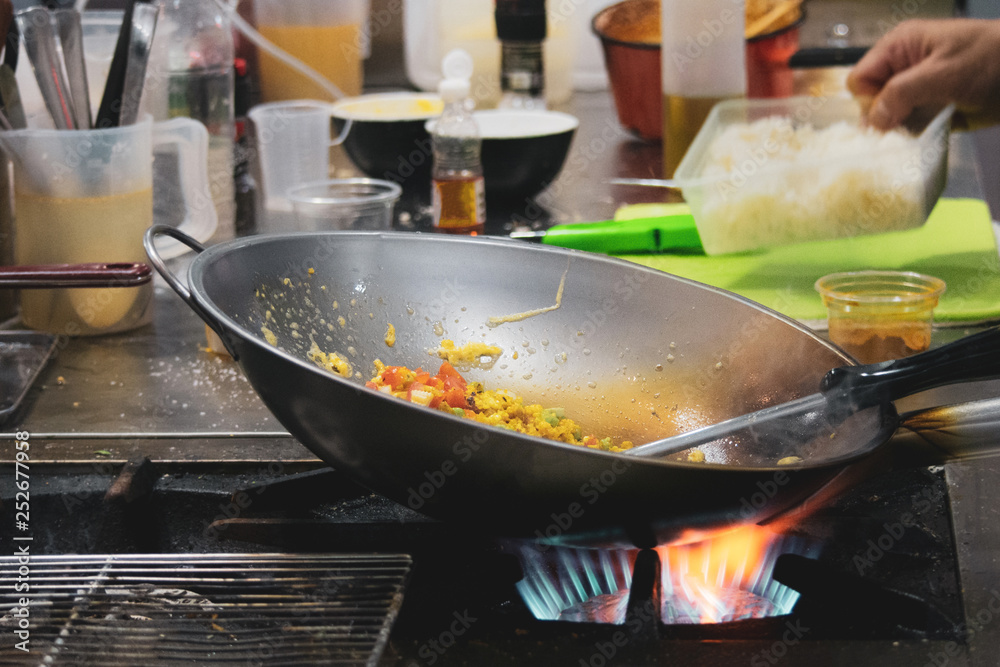 Chef cooking with flame in a frying pan on a kitchen stove, Chef in restaurant kitchen at stove with pan Chef cooking with flame in a frying pan on a kitchen stove, Chef in restaurant kitchen at stove with pan