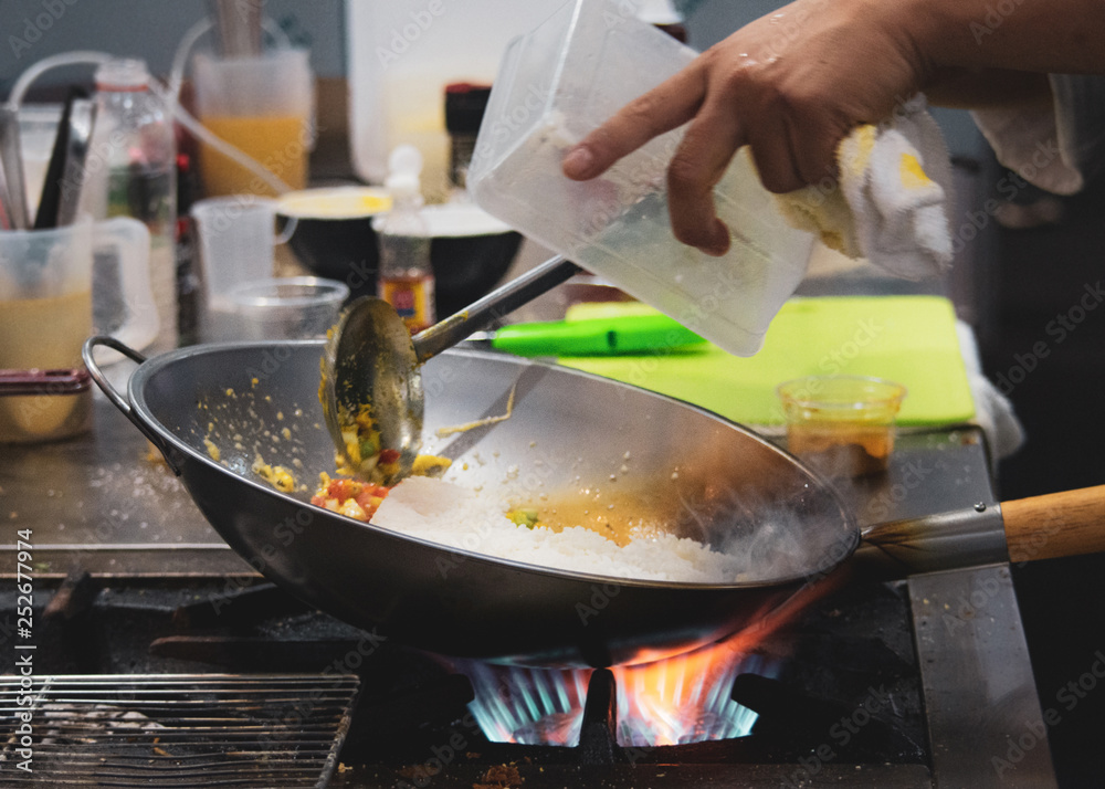 Chef cooking with flame in a frying pan on a kitchen stove, Chef in restaurant kitchen at stove with pan Chef cooking with flame in a frying pan on a kitchen stove, Chef in restaurant kitchen at stove with pan