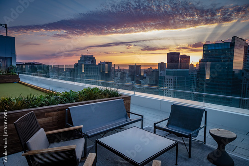 A rooftop deck with chairs overlooks the San Francisco skyline sunset with purple and gold clouds