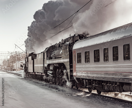 Steam train moves toward at cold winter morning time.