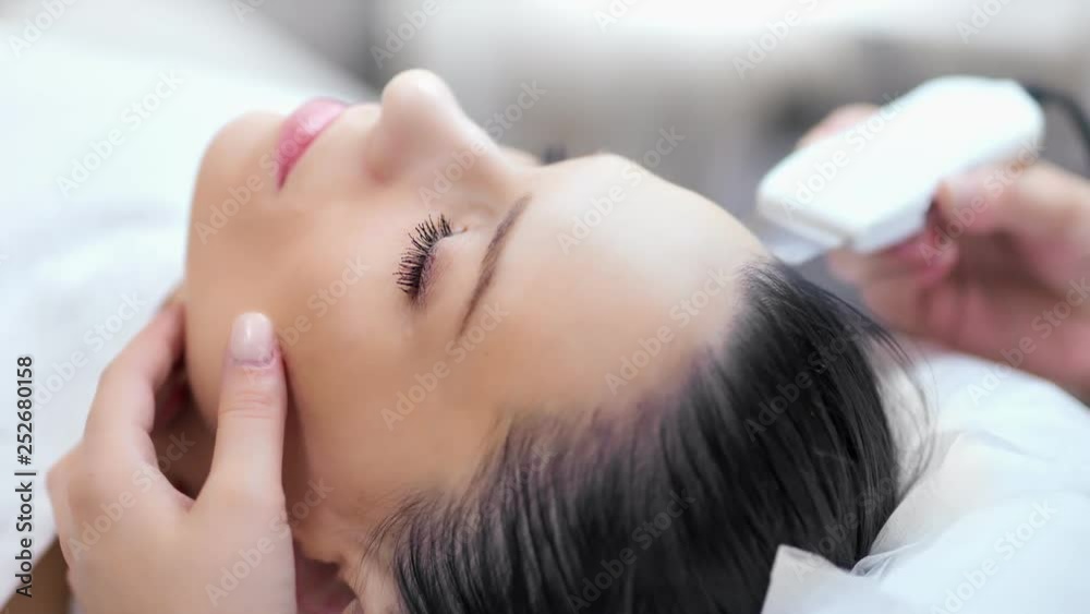 Close-up young charming girl lying on couch during process refresh making ultrasonic peeling Close-up young charming girl lying on couch during process refresh making ultrasonic peeling