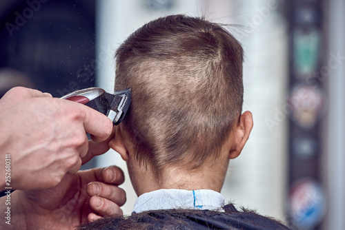 Hairdresser making a haircut to a boy with clipper. Back view.