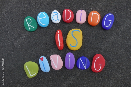 Reading is living, cultural quote with multi colored painted stones over black volcanic sand