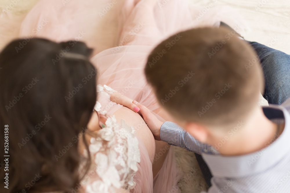 Fototapeta premium pregnant girl in peach-colored negligee. the hands of men and women in the abdomen. 