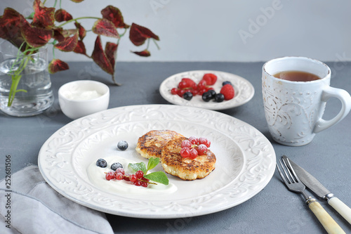 Wallpaper Mural The concept of a delicious breakfast. Cottage cheese pancakes with sour cream and berries. In the plate are red currants, raspberries, blueberries. In the frame cutlery, a cup of tea, napkin. Close-up Torontodigital.ca