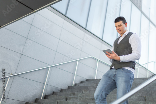 Young and Casual Businessman Using Tablet while Walking Outside of Office Building © 24K-Production