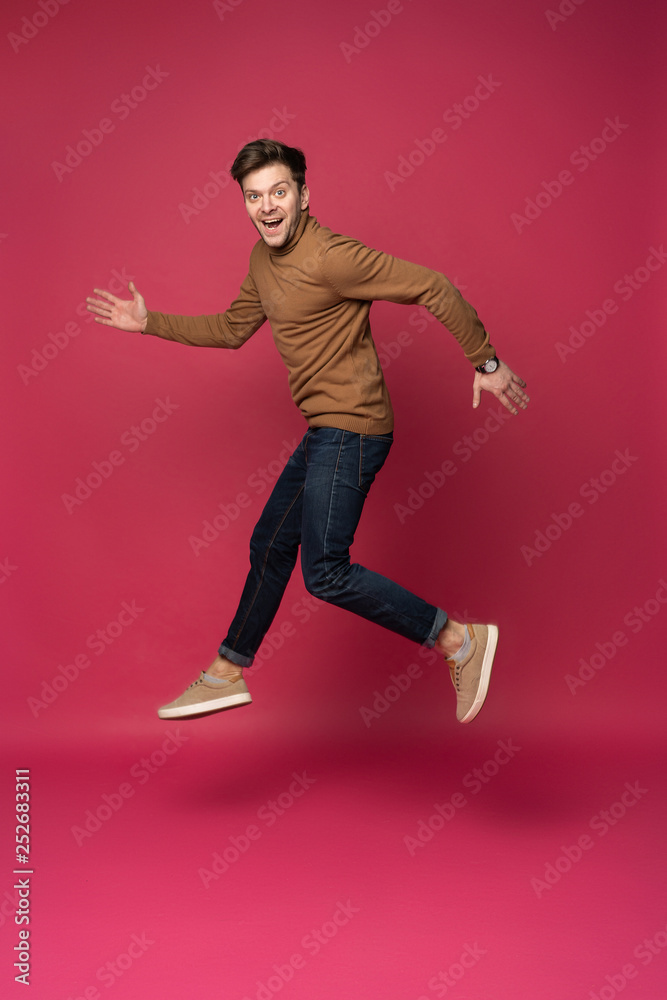 Happy excited cheerful young man jumping and celebrating success isolated on a pink background.