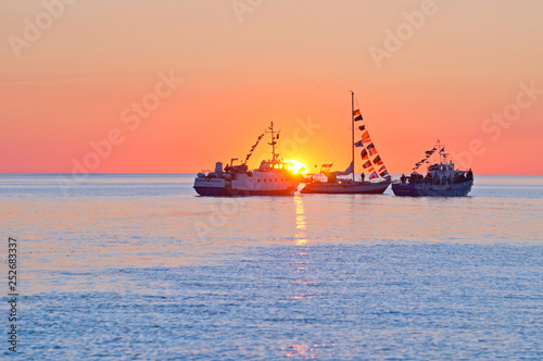 Silhouettes of three ships against the setting sun.
