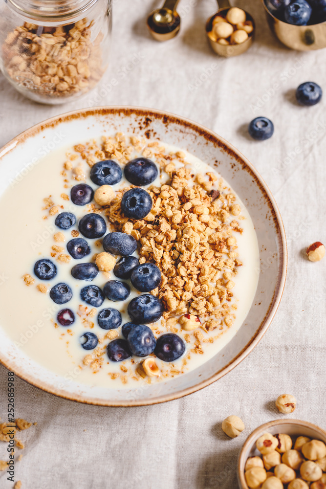Healthy breakfast, a bowl with organic granola, chocolate pieces, fresh blueberries, hazelnuts and soya milk.