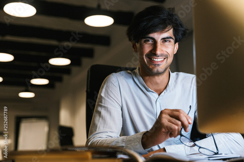 Smiling young man working at the office late at night photo