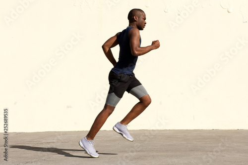 Full body profile  of healthy young african american man running by wall