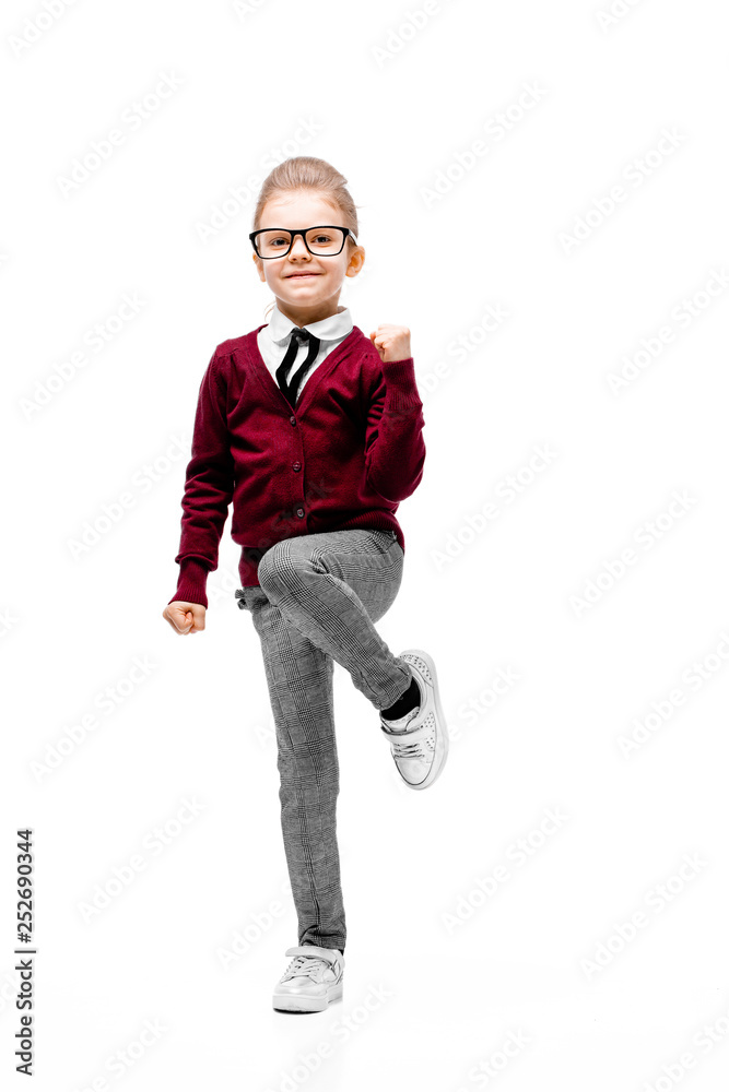 Beautiful little girl dressed like a School girl - in white shirt, red blouse and gray pants, rounded glasses standing near white wall and posing thumbs-up like model. Beautiful little girl dressed like a School girl - in white shirt, red blouse and gray pants, rounded glasses standing near white wall and posing thumbs-up like model.