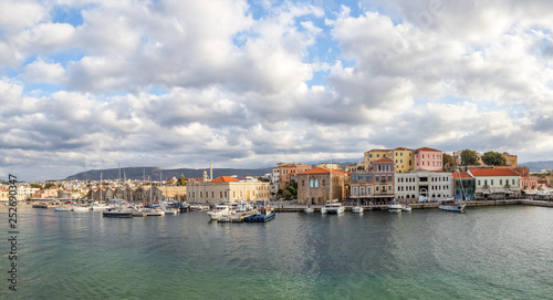 A panorama of the seaport town Chania, the island of Crete, Greece. A harbor with wooden pantons, moored yachts, ships, boats. Colorful architecture of modern and old houses. Mountains on the horizon. © Vitalii_Mamchuk