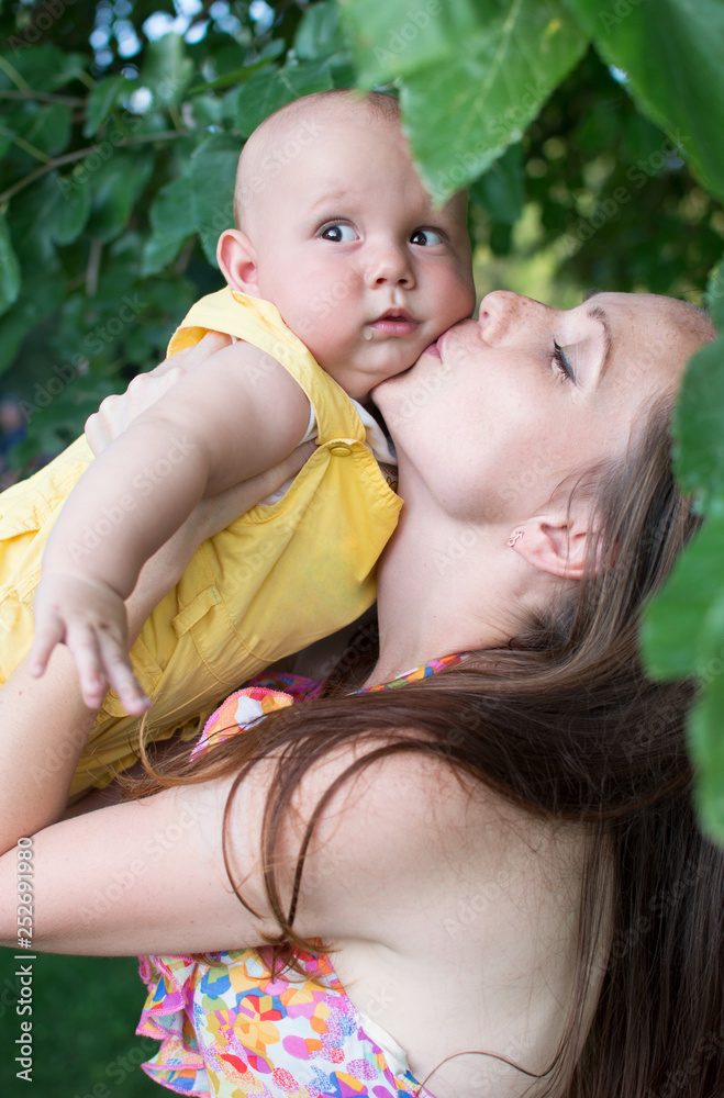 Mom holds the baby in her arms and kisses him in the park. Mom holds the baby in her arms and kisses him in the park.