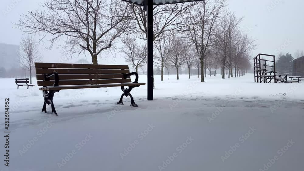 Snowing Scene With Park Bench in Day. Snowy Landscape With Public Park Architecture Under Overcast Sky. Snowing Scene With Park Bench in Day. Snowy Landscape With Public Park Architecture Under Overcast Sky.