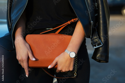 Luxurious young woman in black leather jacket holding orange purse