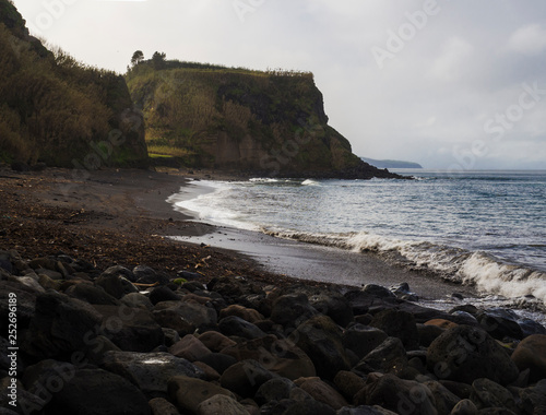 Praia da Viola beach with grassy sandstone cliffs and volacanic rock boulders, atlantic ocean landscape, Sao Miguel island Azores island Portugal