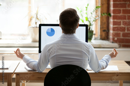 Quadro em tela Rear view businessman sitting at desk opposite pc doing yoga
