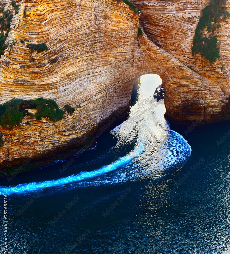 Fototapeta premium bateau à moteur passant sous le rocher aux pigeons symbole de Beyrouth, Liban, en laissant un sillage blanc dans l'eau bleu marine