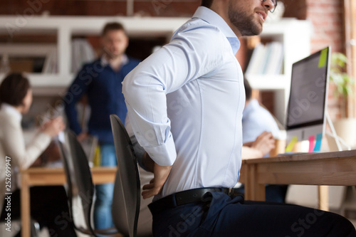 Businessman suffers from lower back pain sitting in shared office