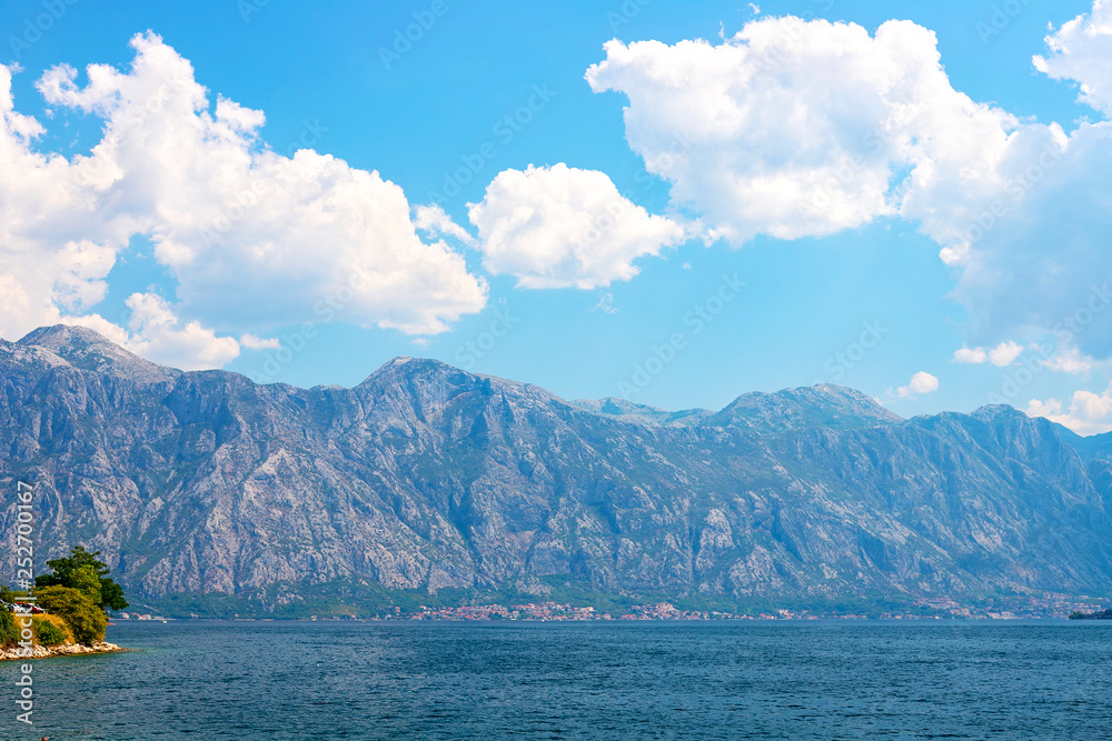 Incredible bright seascape. View of green wooded mountains and blue sea, blue sky and white clouds. Boka Kotorska Bay, Montenegro Incredible bright seascape. View of green wooded mountains and blue sea, blue sky and white clouds. Boka Kotorska Bay, Montenegro