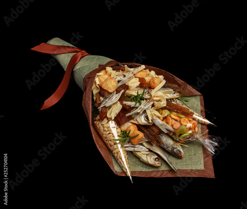 Original bouquet consisting of dried salted fish, salted peanuts, crackers, dried bread and other beer snacks isolated on black background as male gift. Left view photo