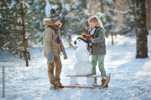 Children build a snowman. Boys building a snow man playing outside on a sunny snowy winter day. Outdoor family holiday on the Christmas holidays. Boy and girl playing snowballs.