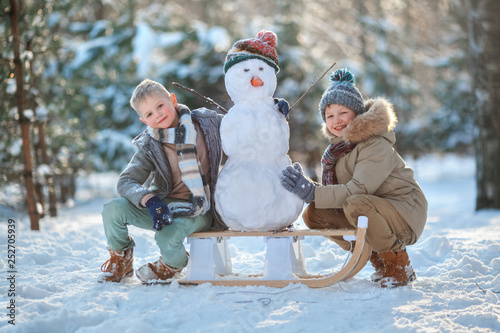 Children make a snowman. Children building a snow man playing outside on a sunny snowy winter day. Outdoor family holiday on the Christmas holidays. Boys play snowballs. Winter clothes photo