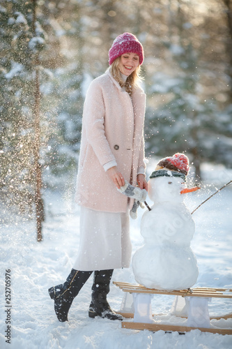 A happy family! Woman on a winter walk in nature molds a snowman in a sunny day. Winter vacation