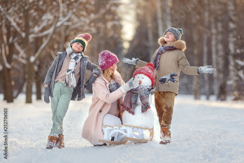 Mom and children in the winter forest play snowballs and make a snowman. Walking in the winter holidays.