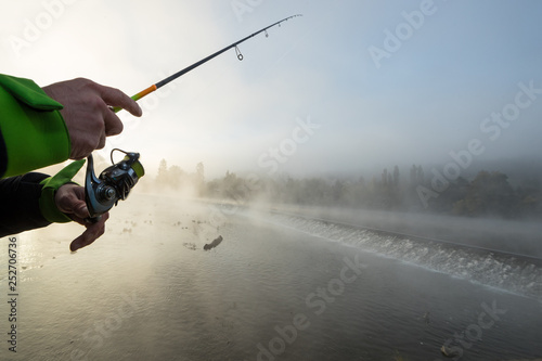 Man fishing in river with fly rod during summer morning. Beautiful fog.