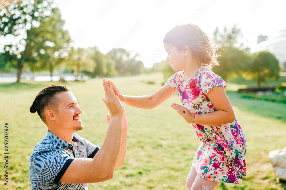 Fototapeta premium Dad and daughter summer outdoor activity. Loving father adore his lovely playful baby. Parent and child have fun in park. Carefree childhood. Happy family lifestyle portrait. Cheerful girl clapping