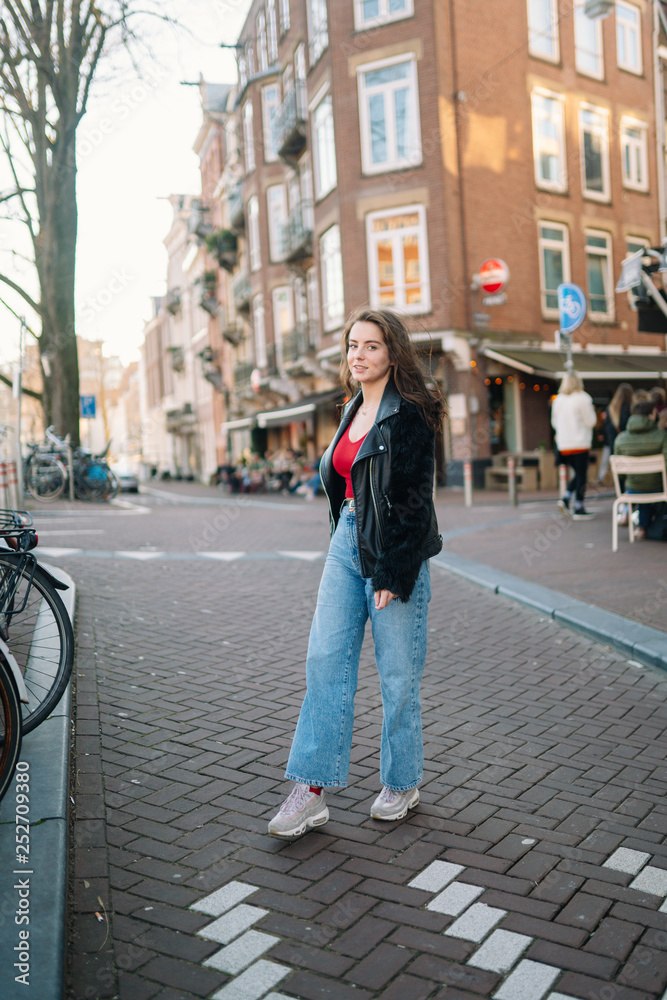 Portrait of a beautiful girl on a sunny day. Streets of Amsterdam. Great mood. A girl enjoys her lifestyle. She is wearing a red T-shirt, jeans and a leather jacket.