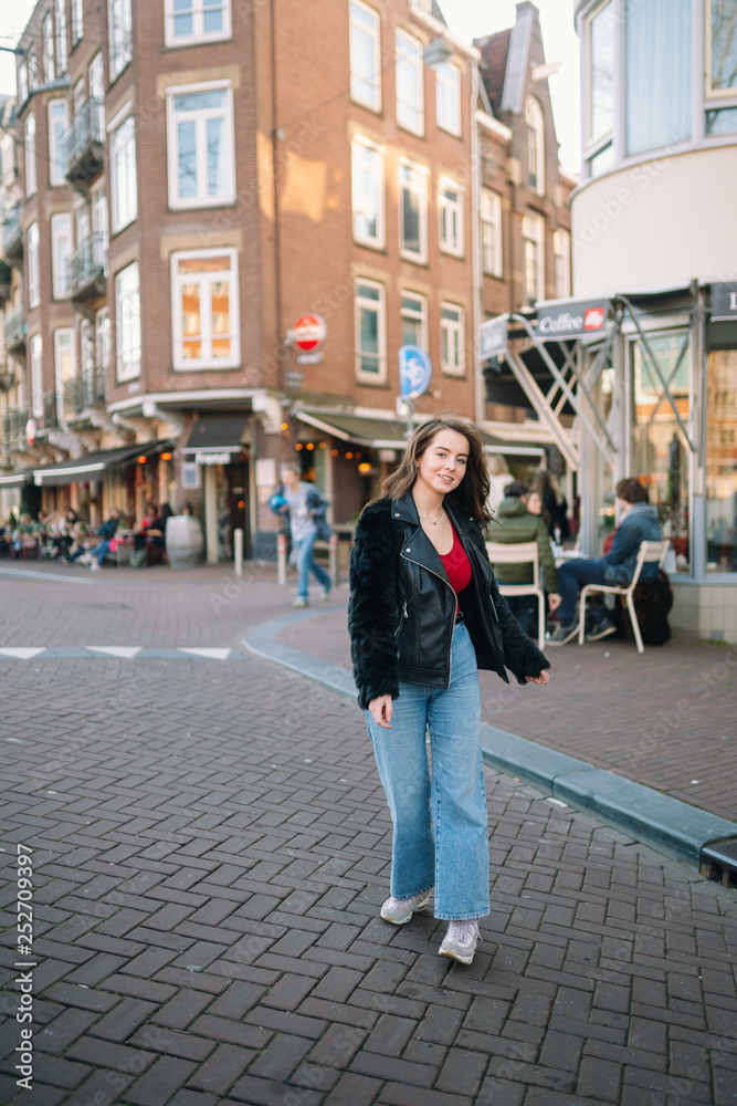 Portrait of a beautiful girl on a sunny day. Streets of Amsterdam. Great mood. A girl enjoys her lifestyle. She is wearing a red T-shirt, jeans and a leather jacket.