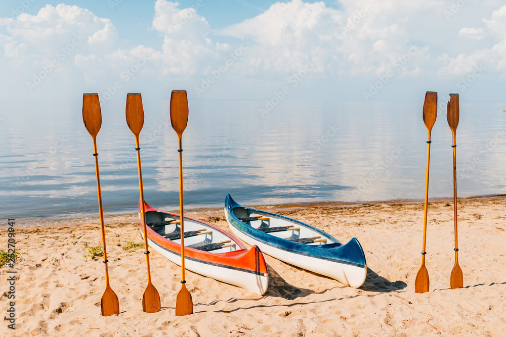 Canoe on beach in sunny summer day on blurred sea with clouds background. Kayak with wooden paddles on coast of mediterranean sea. Summer adventure. Travel, tourism, vacation concept. Boat rent. Canoe on beach in sunny summer day on blurred sea with clouds background. Kayak with wooden paddles on coast of mediterranean sea. Summer adventure. Travel, tourism, vacation concept. Boat rent.