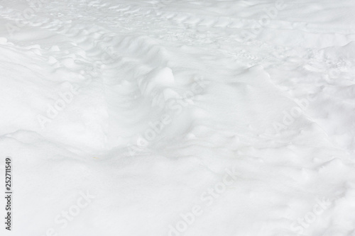 Fresh white snow with traces from the tractor. Abstract background with a snowy texture.