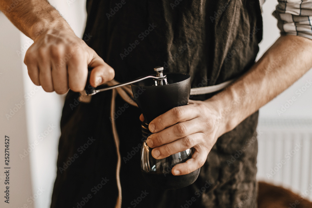 Hands holding manual grinder  with coffee beans. Items for an alternative coffee. Professional barista in black stylish apron grinding coffee for aeropress, alternative brewing method