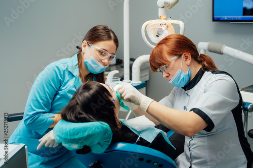Dentist woman and her assistant in medical clothes treating patient's teeth in a stomatological centre. Dental cure. Toothcare concept