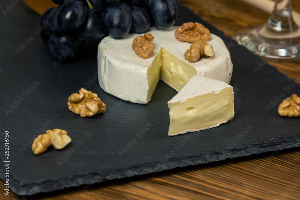 Camembert cheese in a dark tray next to sweet blue grapes nuts and honey