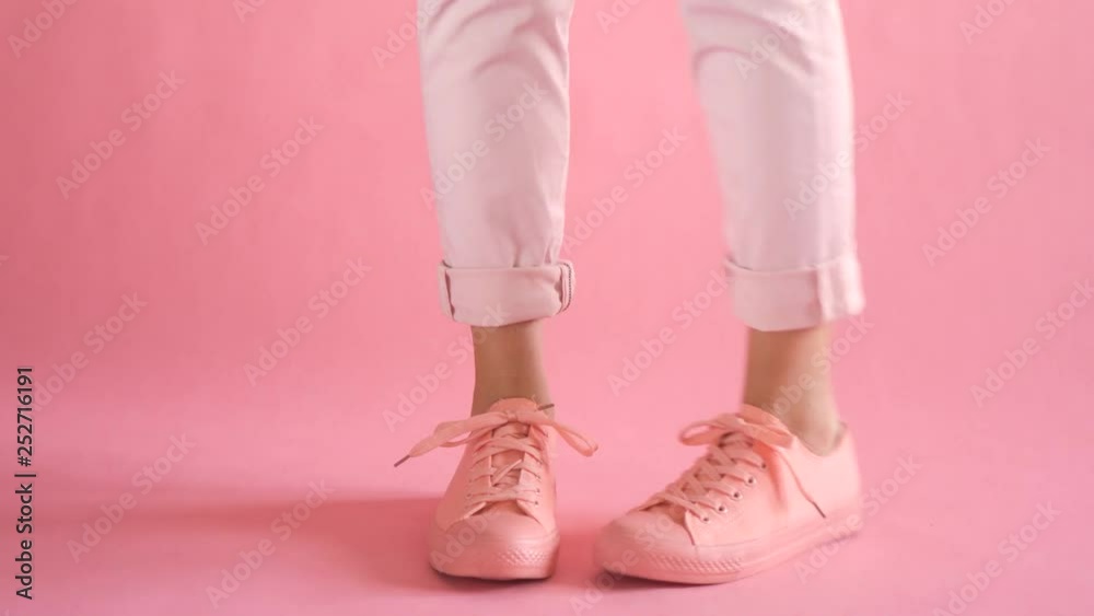 Close up of shapely young female legs walking in fashionable sneakers on coral background Close up of shapely young female legs walking in fashionable sneakers on coral background