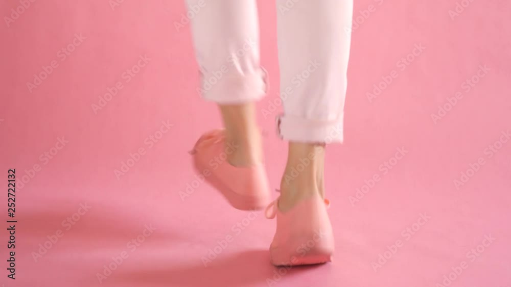 Close up of slim female legs dancing in fashionable sneakers on coral background Close up of slim female legs dancing in fashionable sneakers on coral background