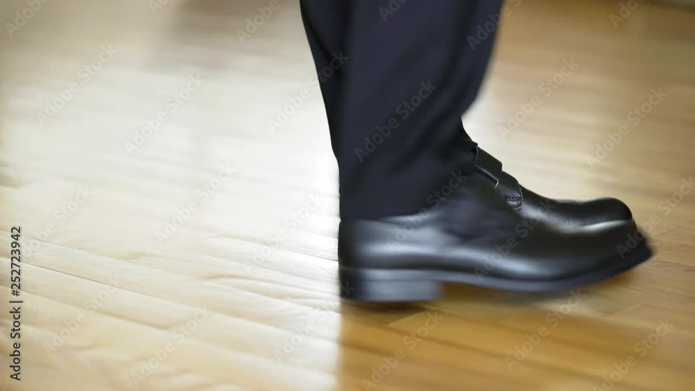 Man's legs with suit trousers and black leather shoes walking on the wooden floor. Young male walks on a spot and shows his new shoes.Close-up Man's legs with suit trousers and black leather shoes walking on the wooden floor. Young male walks on a spot and shows his new shoes.Close-up