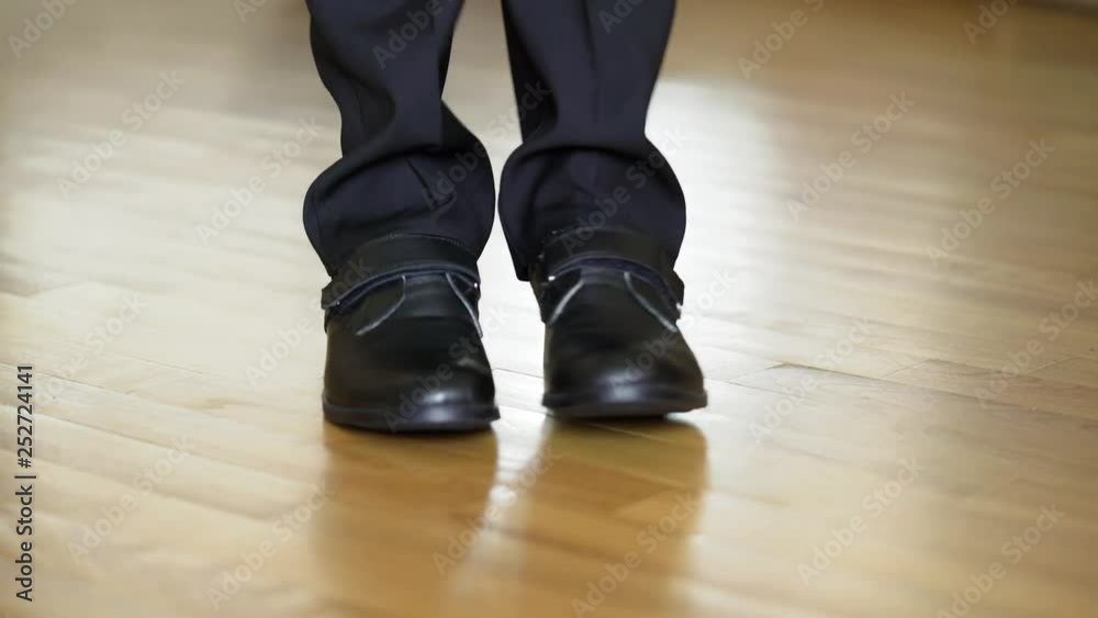 Man in black leather shoes dancing on the wooden floor. Male's legs in black trousers and new shoes shows some kind of dance on a parquet. Close-up Man in black leather shoes dancing on the wooden floor. Male's legs in black trousers and new shoes shows some kind of dance on a parquet. Close-up